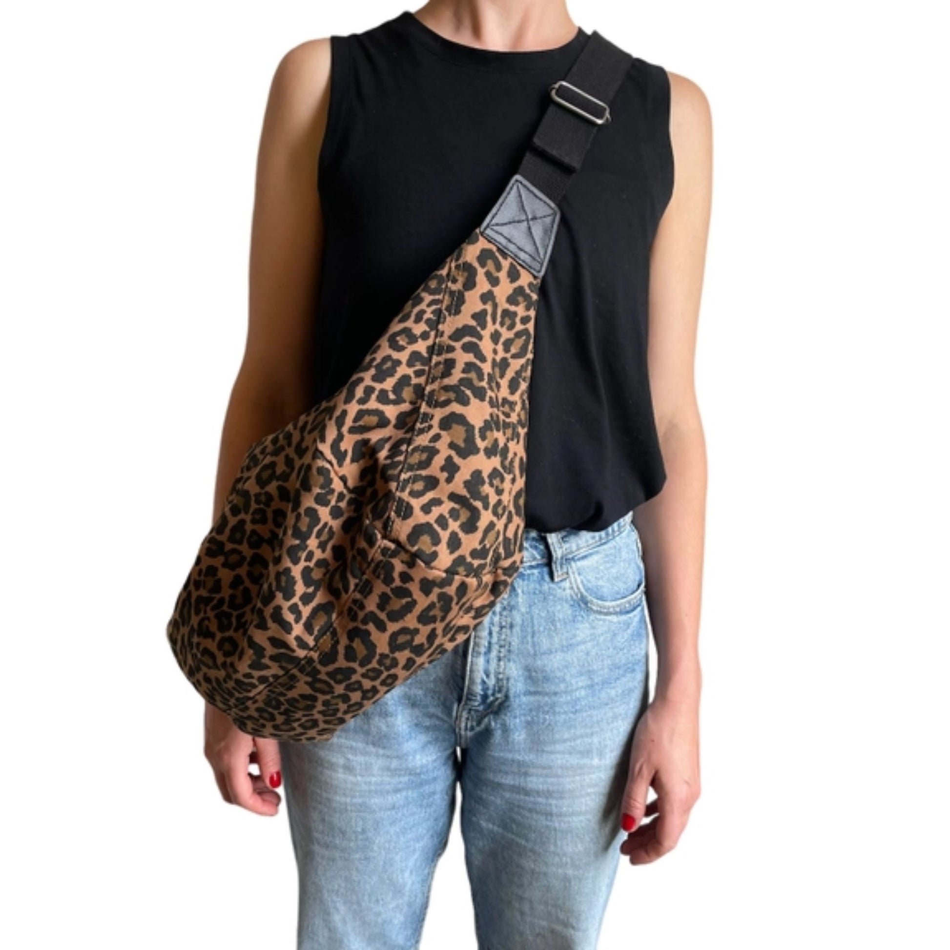 Person wearing a large leopard print cross body sling bag over a black sleeveless top and jeans.