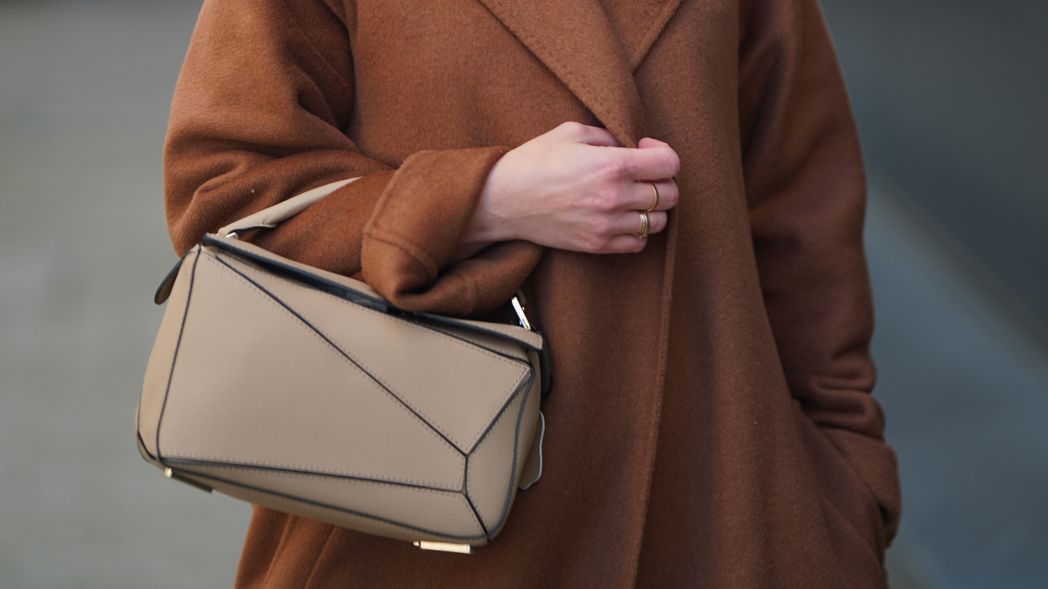 Woman wearing a brown coat and sunglasses, holding a beige handbag.