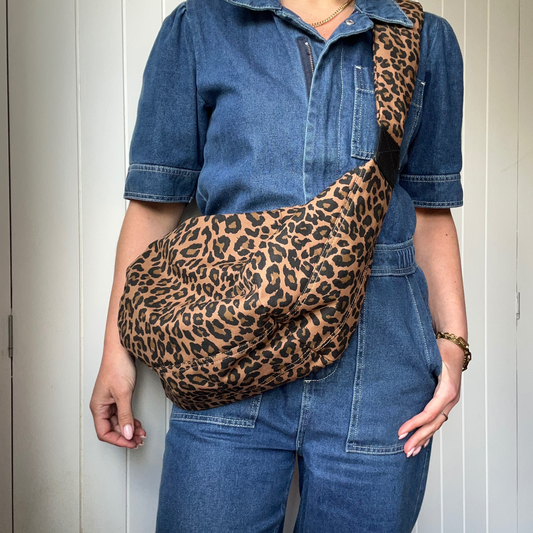 Person wearing a large leopard print cross body sling bag over a denim jumpsuit.