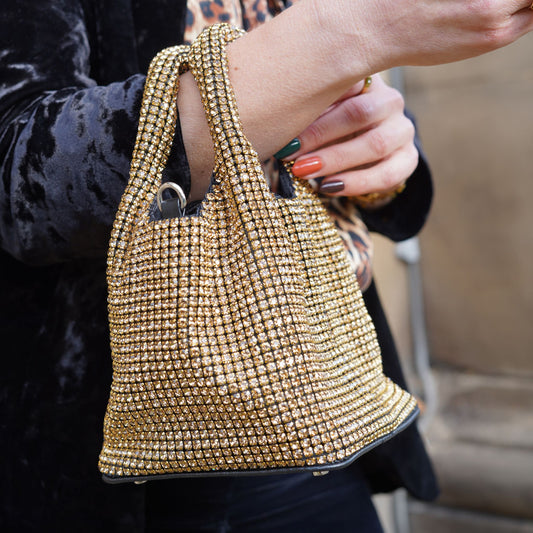 Close-up of a person holding a gold crystal-covered handbag with double grab handles