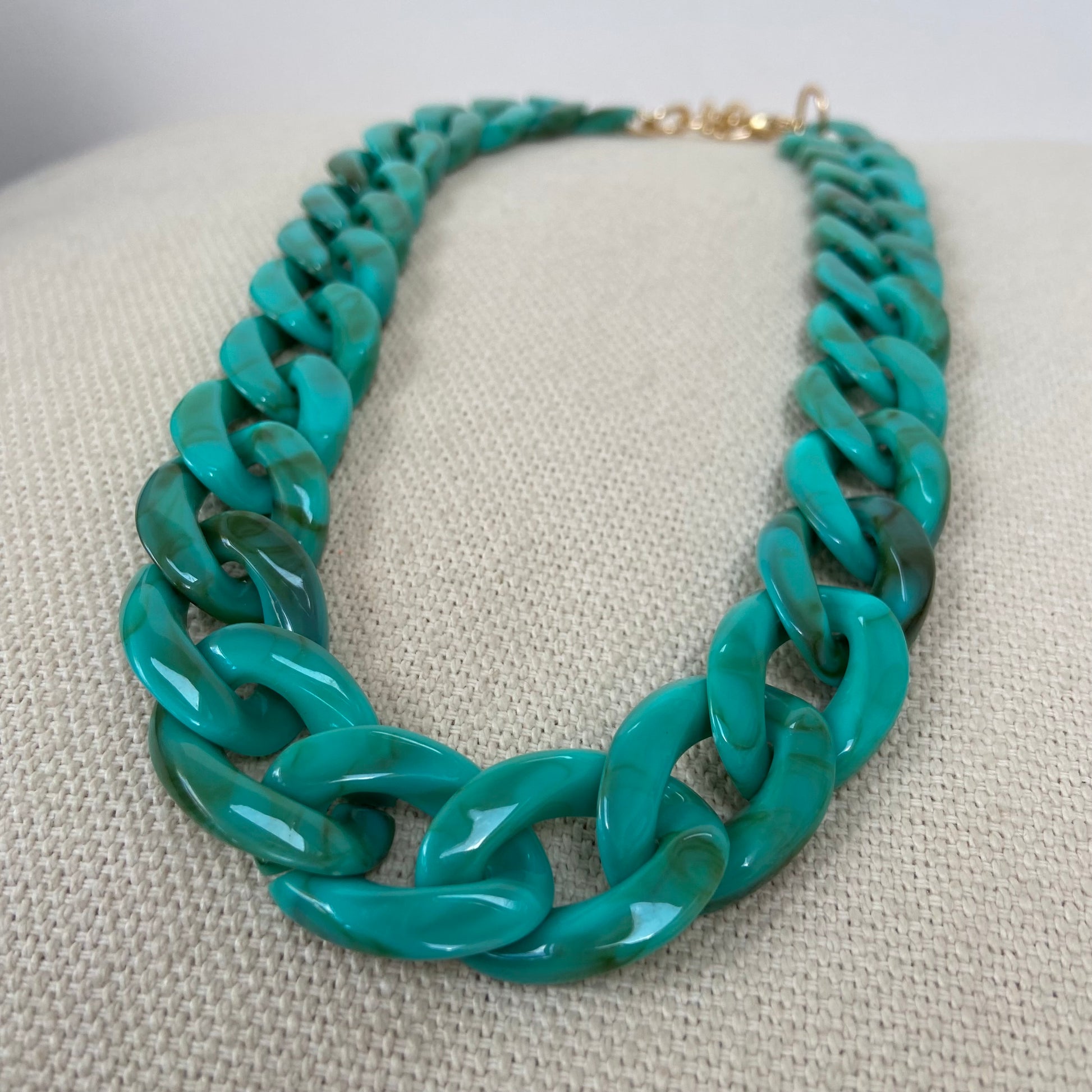 Close-up of a green chunky link statement necklace displayed on a beige fabric surface