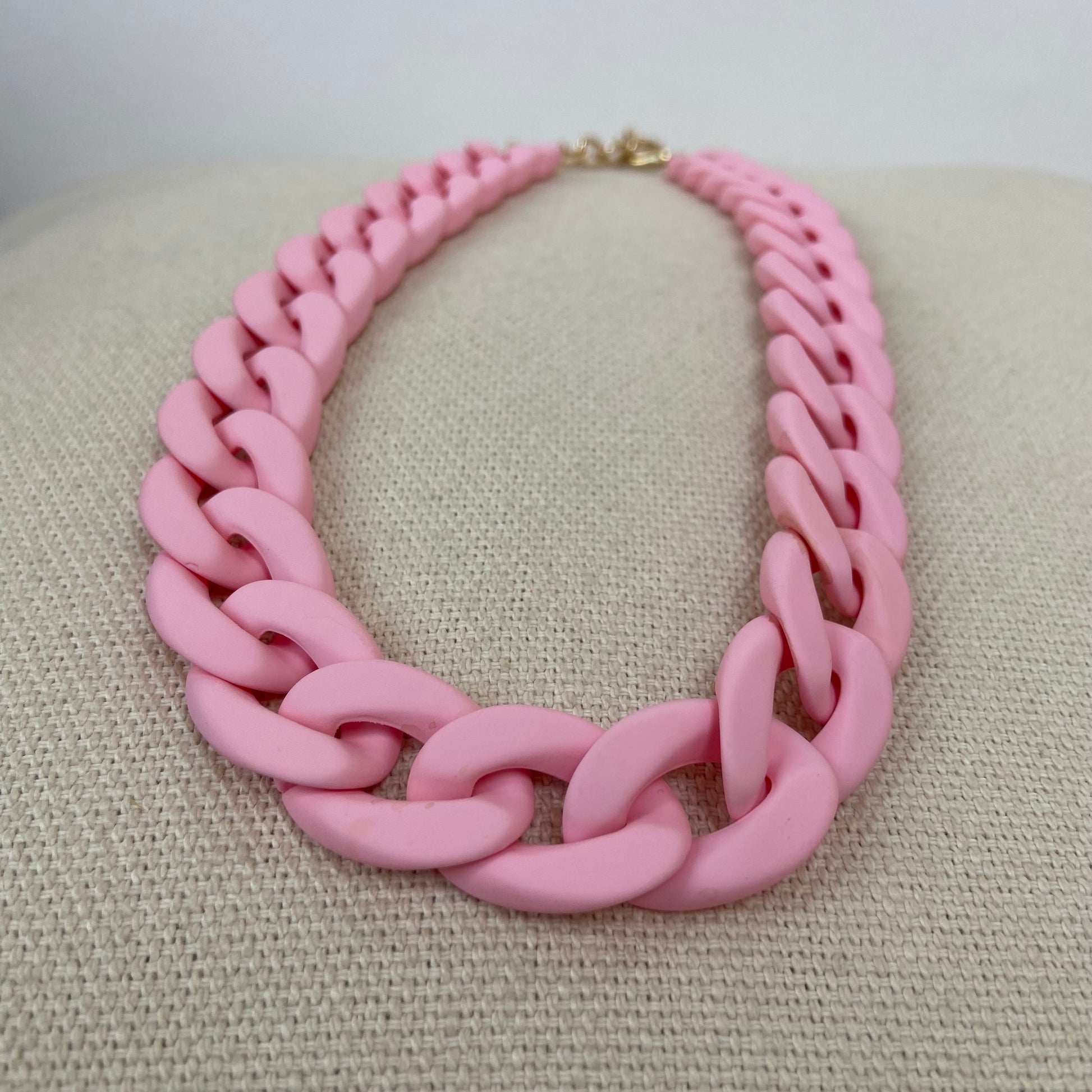 Pink chunky link statement necklace displayed on a beige fabric background.