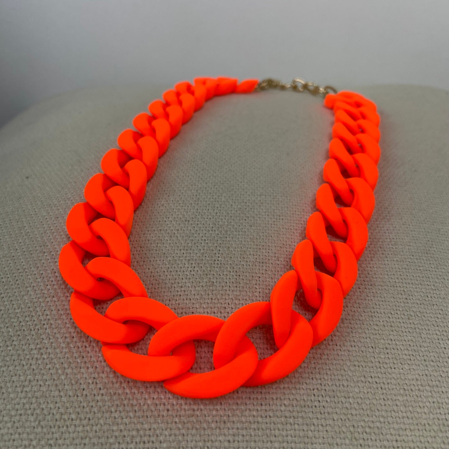 Neon orange chunky link statement necklace displayed on a beige surface.